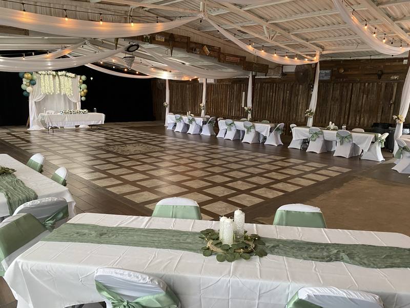 Long tables with sage runners and white chairs across the open dance floor