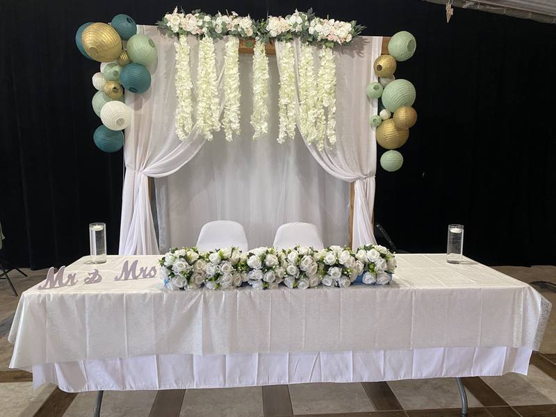 Head table with balloon garland and flowers in front of a draped backdrop